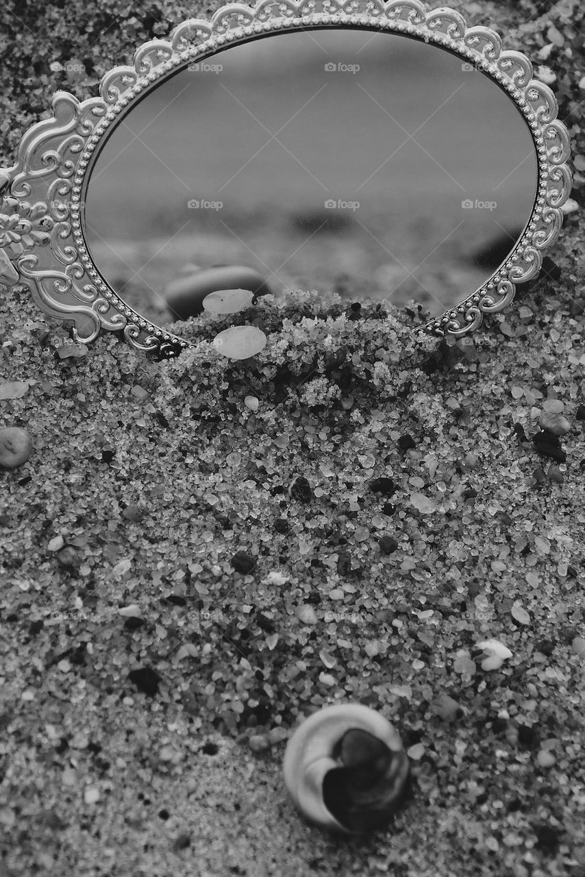 Monochrome beach mirror image, shells and rocks being reflected in the mirror, seeing the beach through reflections, black and white reflections, not ordinary reflections 