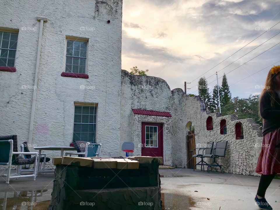 White and red spanish old style architecture residential large house built in the early 1900s. Dark wine red door with window on the side with aging signs with stairs style wall before sunset with sunlight on top of old nice well.