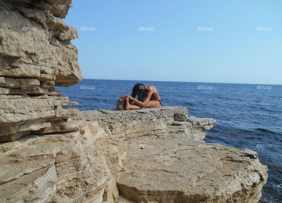 girl training yoga on a sea stone shore summer time