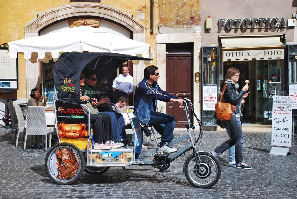 Bike taxi in Rome. A bike taxi takes tourists along the roman cobblestone streets as a pedestrian eats gelato in a cone 