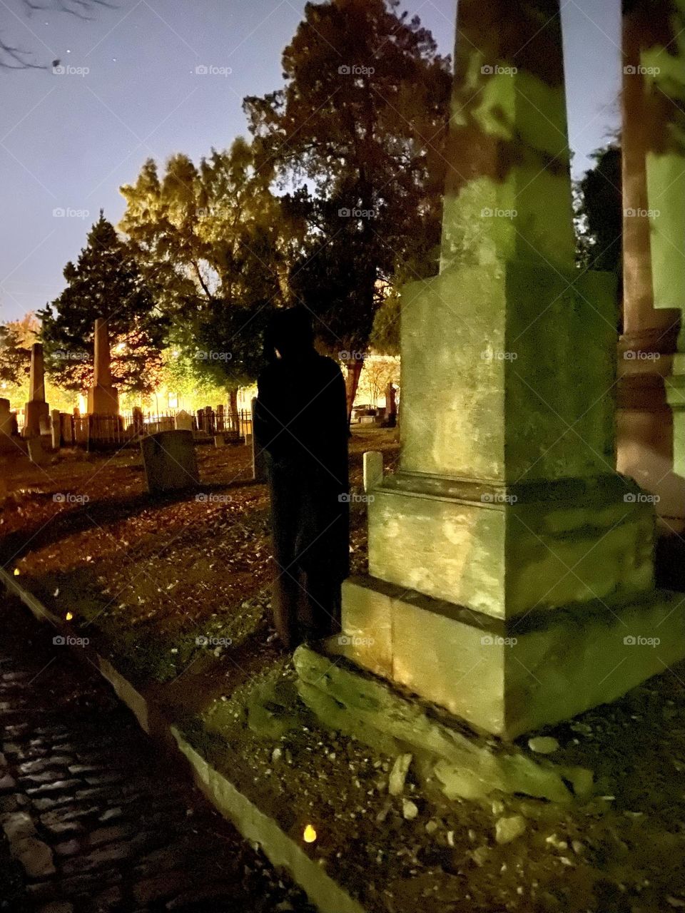 Cloaked figure by gravestone at night 