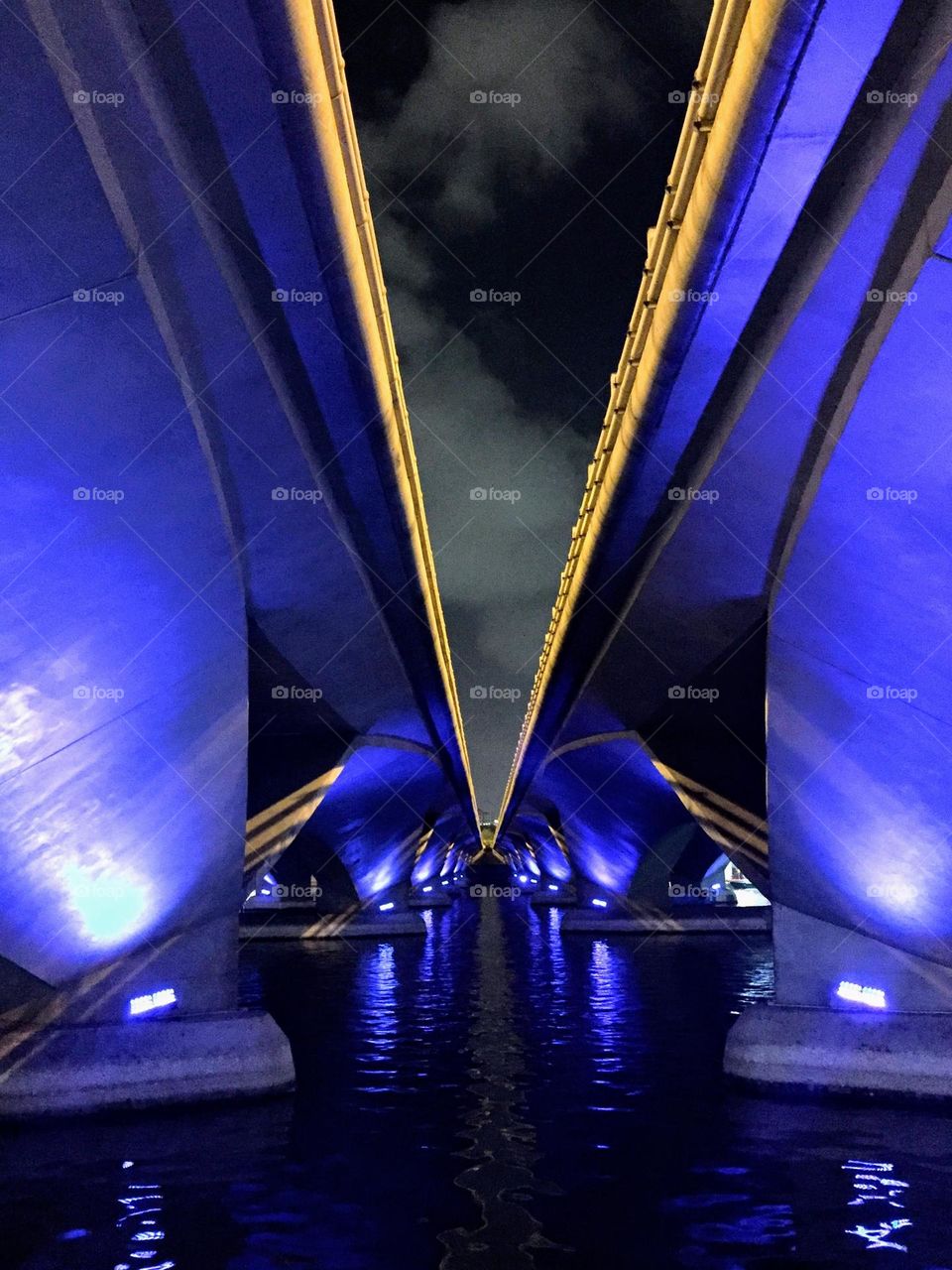 Two parallel blue lighted bridges over the water bottom view