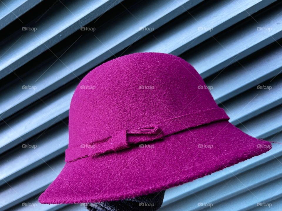 A person holding a magenta hat against light blue green background.