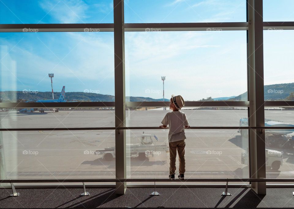 Little boy in straw hat staying near big window.  Kid in an airport