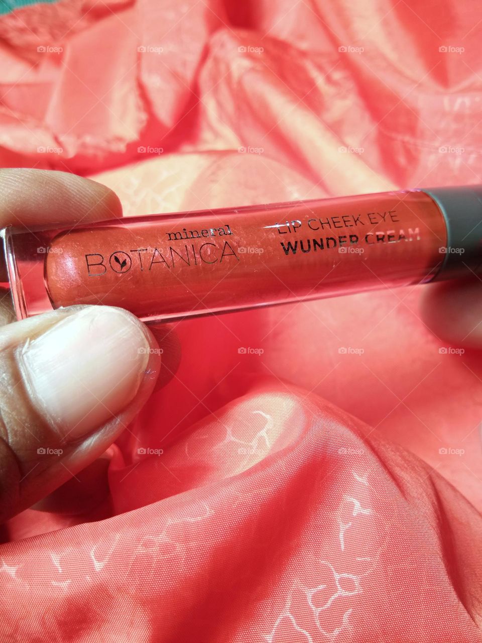 closeup of multi function lip cream on hands. can be used as lip cream, cheek blush and eyeshadow