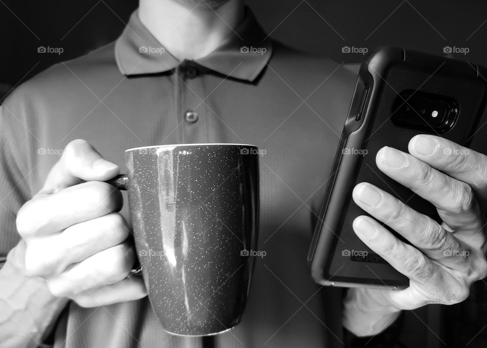 Closeup of a man wearing a polo shirt and drinking coffee while on his cell phone in black and white.