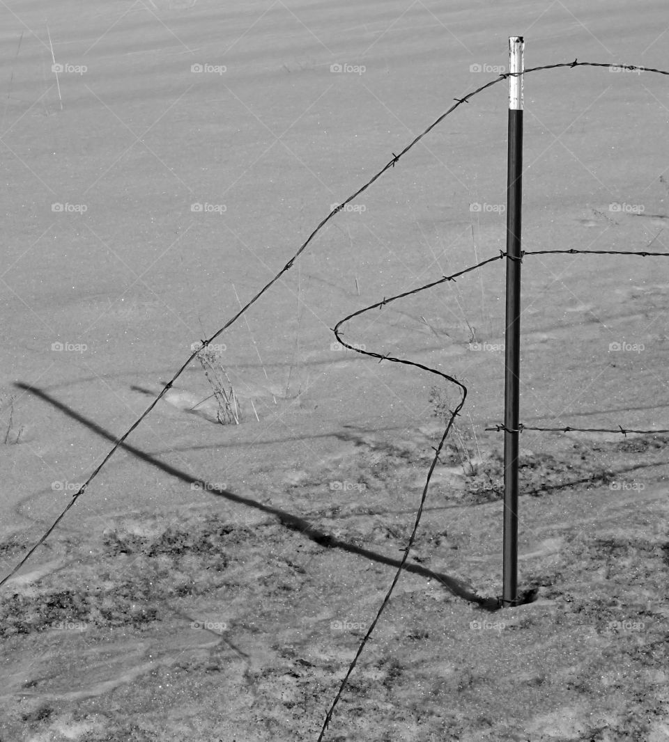 A barbed wire fence on a metal post falling apart in the snow on a winter day in rural Central Oregon. 