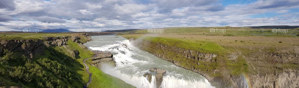 Incredible panorama view of an Icelandic waterfall with a small rainbow