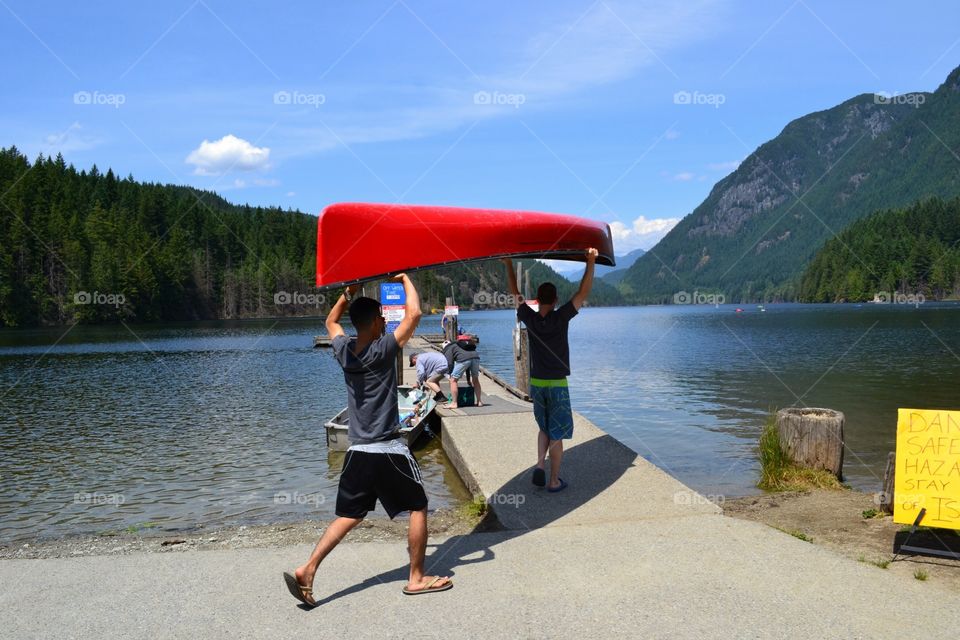 Carrying the kayak.... Male youth carrying a red kayak to dock for lake trip