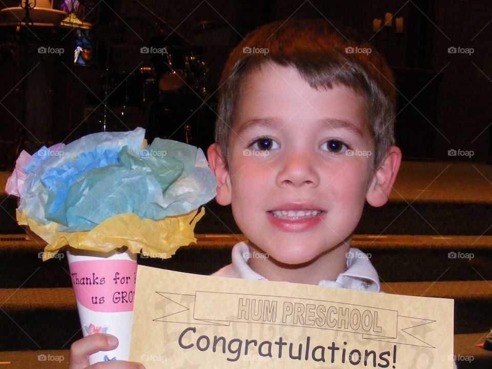 Young boy holding his Preschool graduation certificate