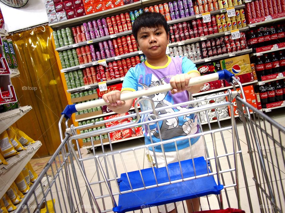 a young boy pushes a grocery cart inside a grocery store