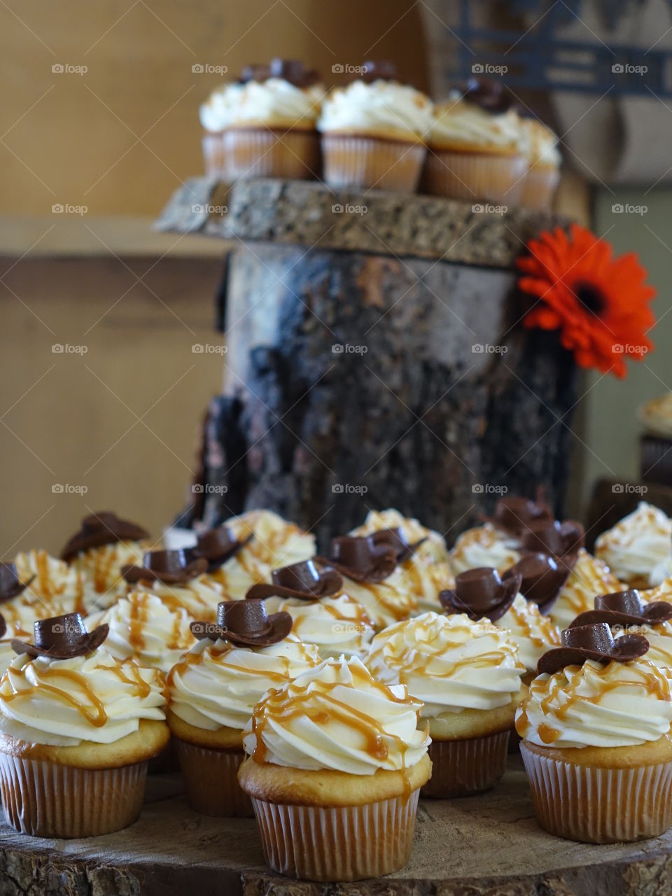 Frosted cupcakes with caramel drizzle and decorated with chocolate cowboy hats lined up by a post. 