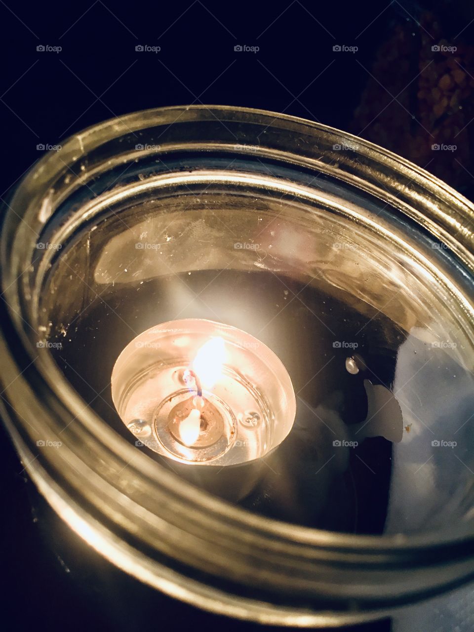 A little candle burning at the bottom of the glass jar