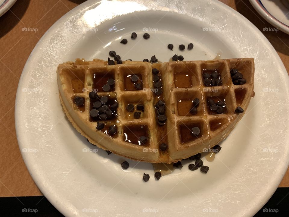 Half waffles on a white round plate with chocolate chips and syrup on a table for breakfast and brunch.