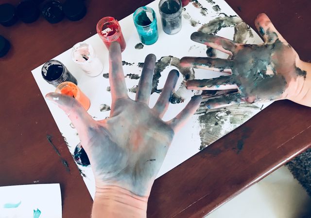 School art project using paint - mother and son showing messy hands and hand prints after creating a picture with brightly colored finger paints