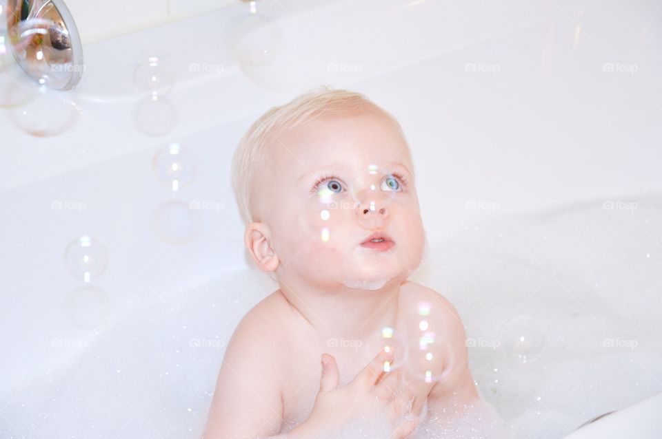 Baby playing in the bath and look to the bubbles
