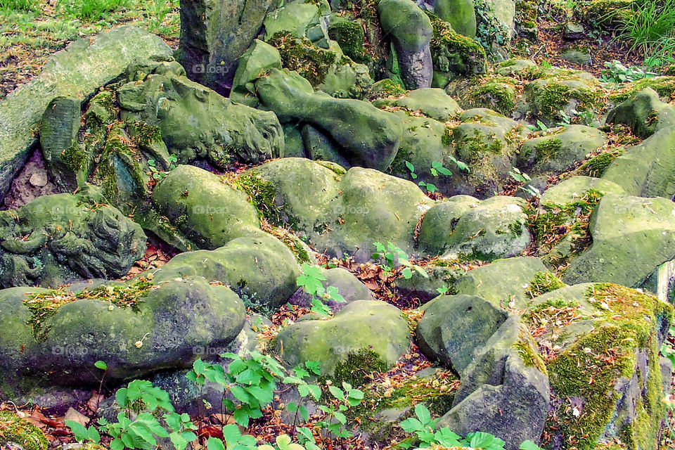 Schlafende Titanen, liegende Steinfiguren mit Moos bedeckt, dazwischen Pflanzen und Laub