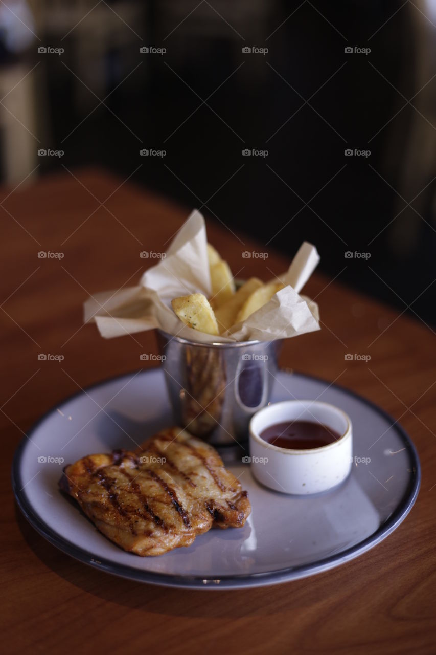 Delicious grilled chicken BBQ and french fries served on plate at a restaurant