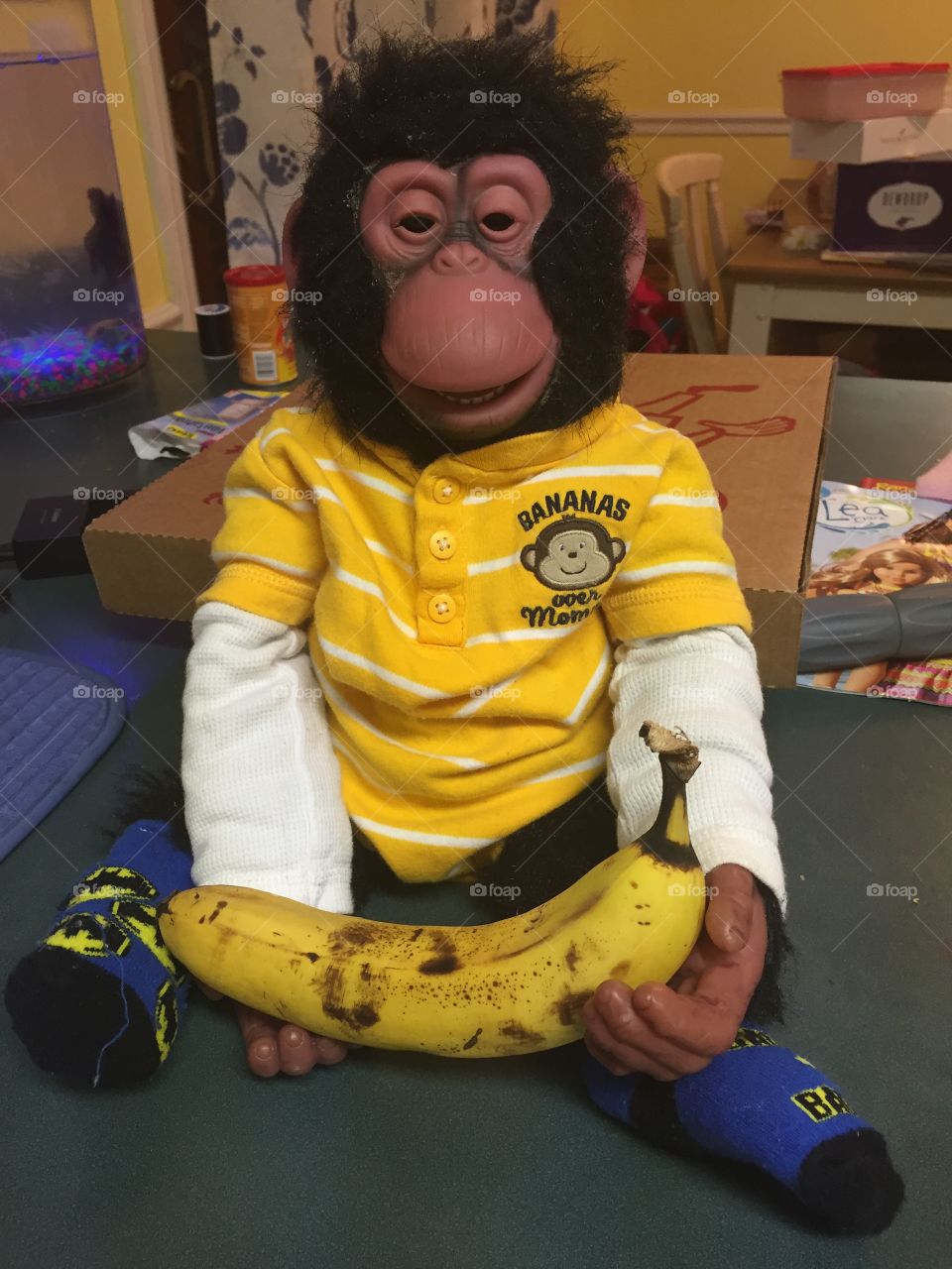 An adorable toy chimp, dressed in a baby onesie, holding a banana. 