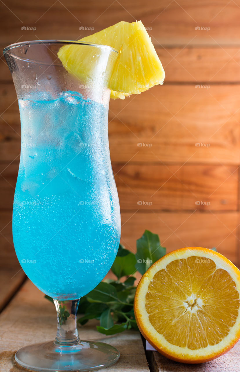 refreshing blue sparkling drink with orange garnish on a wood table in front of a wood background that has a warm orange glow