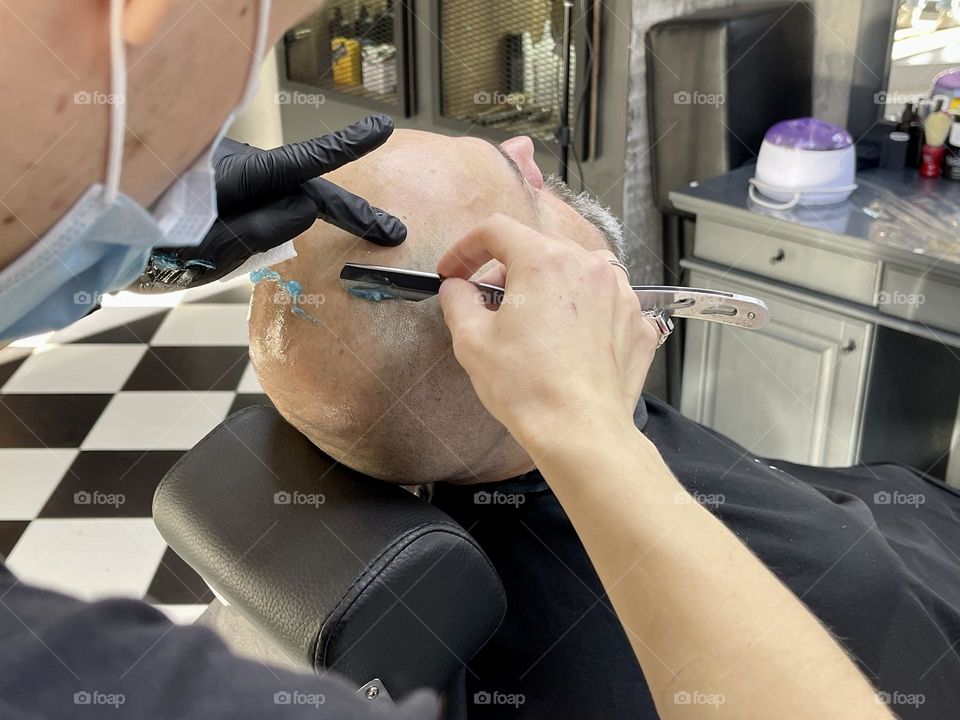 Barber shaving head of client with a straight razor