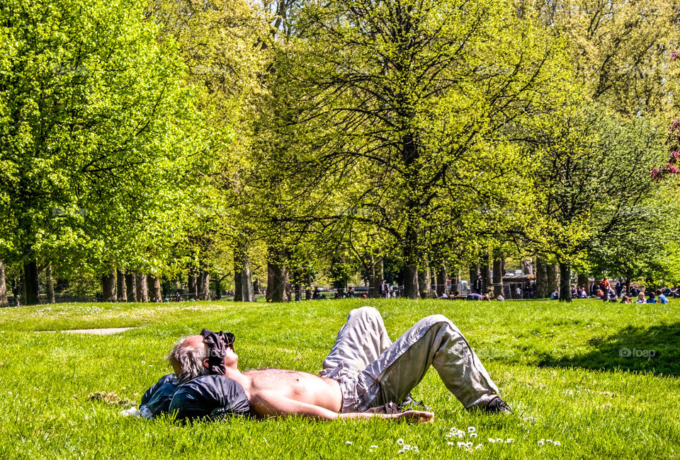 A man sunbathes in London’s Green Park on a hot summer’s day. He has taken his shirt off and put it over his face to shield his eyes from the sun