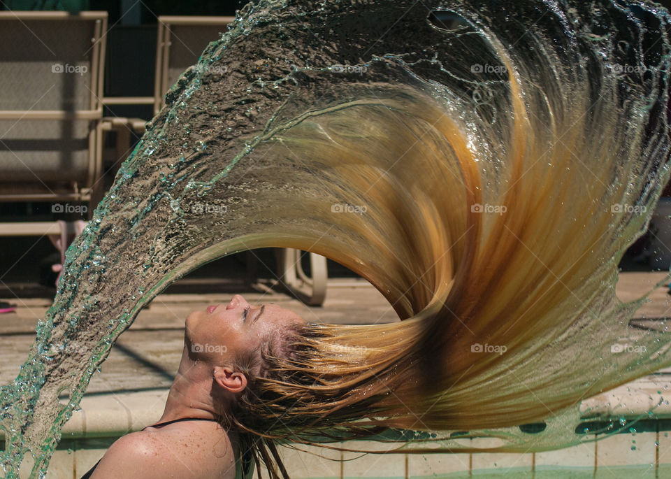 girl with long hair tossing her hair full of water creating a buzz saw design of hair and water