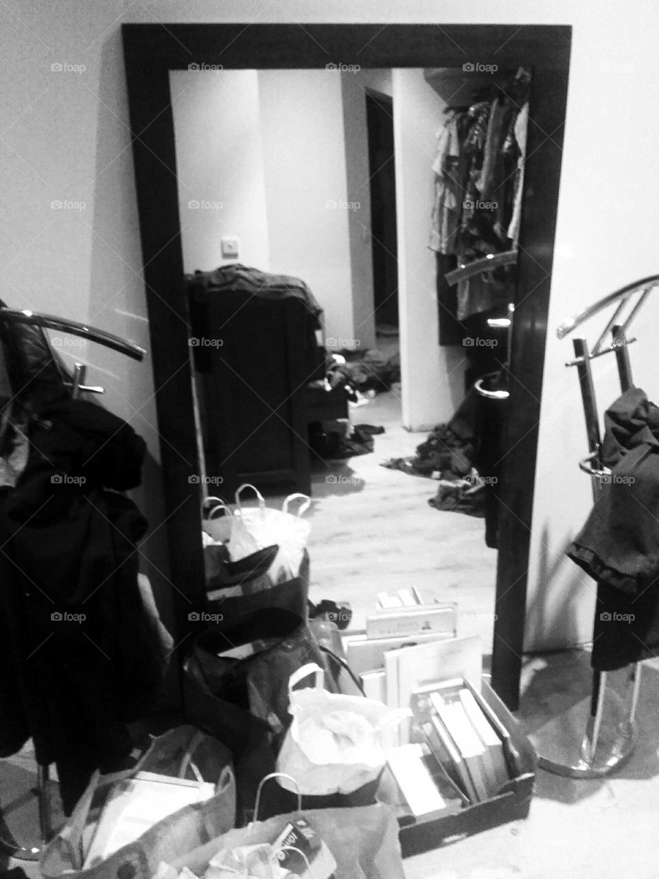 Messy dressing room floor - bags of clothes, boxes of books and various items of clothing  strewn on dressing room floor, with a clear pathway in between all the untidiness captured in a timber framed mirror.