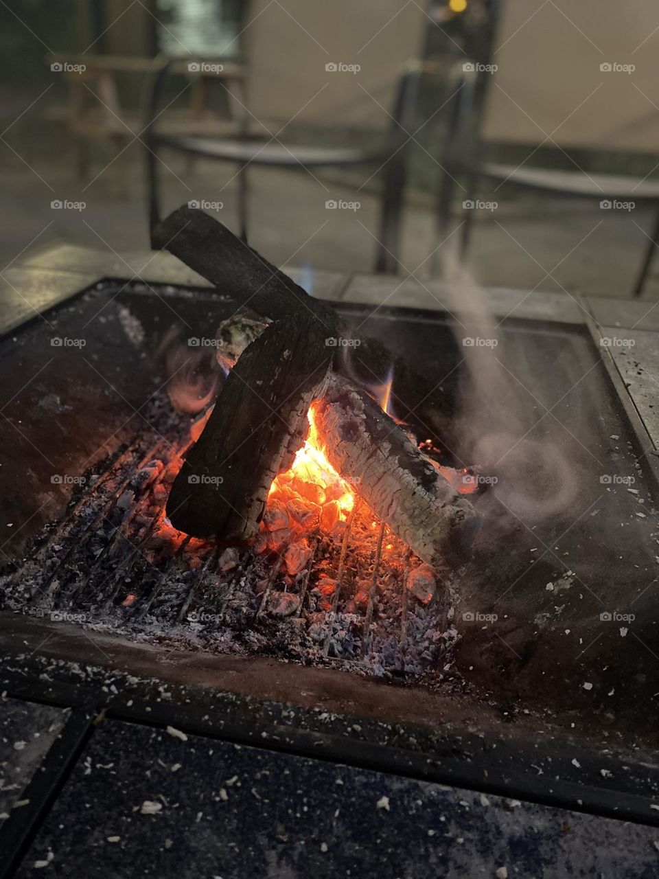 This is a photo of a campfire with burning logs. The embers and flames show a mix of red, orange, and blue colors, indicating the high temperature and presence of different chemicals.