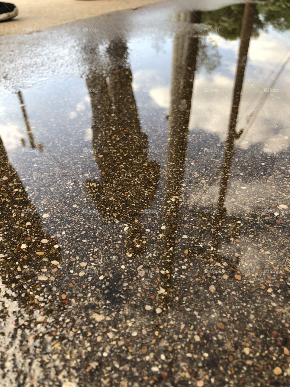 Person reflected in puddle with brown pebbles