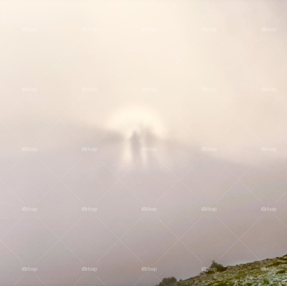 Shadows of hikers cast onto the clouds from a low setting sun while at alpine altitudes 