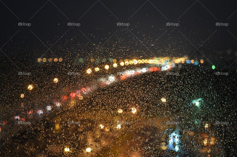Car lights behind window glass with drops of rain.
