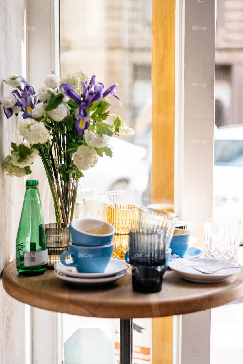 Beautiful flowers in a vase in a coffee shop, surrounded by empty coffee mugs and water glasses.