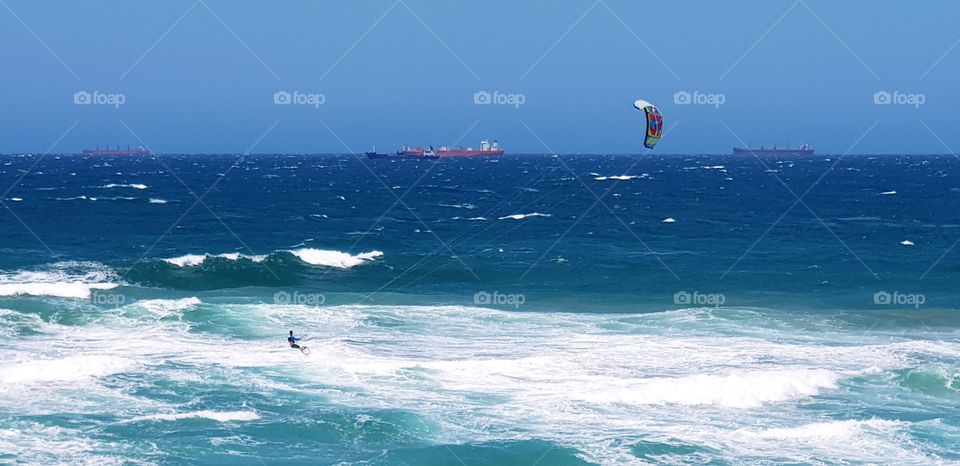 Kitesurfer taking advantage of the gusty wind at Umhlanga Beach with choppy seas, blue skies & a ship in the distance.