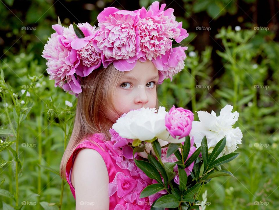 A girl in a pink dress and a wreath of pink peonies.