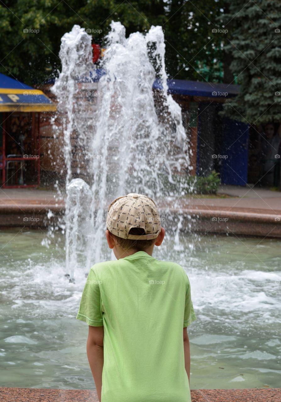 child boy and water splash fountain, summer time, city street view