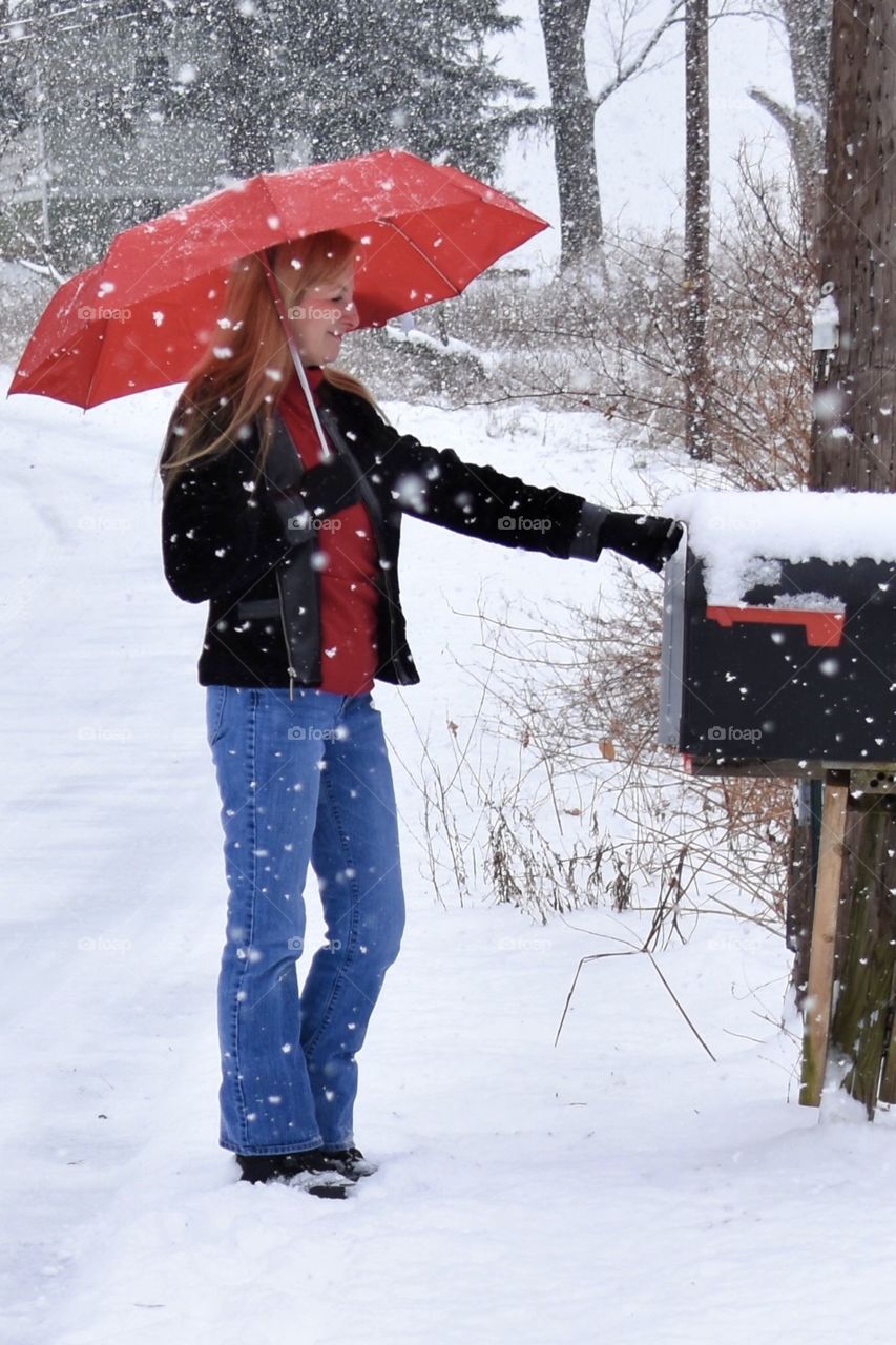 Checking the mail during a snow storm, woman with a red umbrella