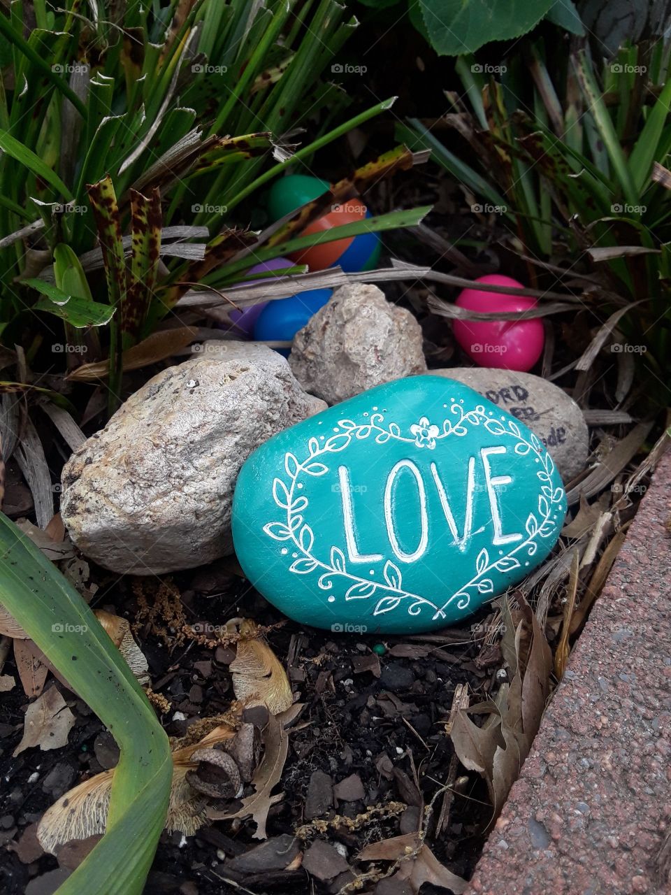 Rocky garden scene with colorful Easter eggs partly hidden.