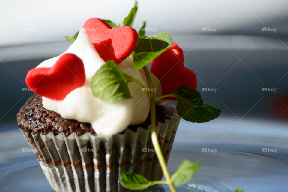 Beautiful cupcake in golden hour sunlight with three hearts and fresh mint in white buttercream frosting 