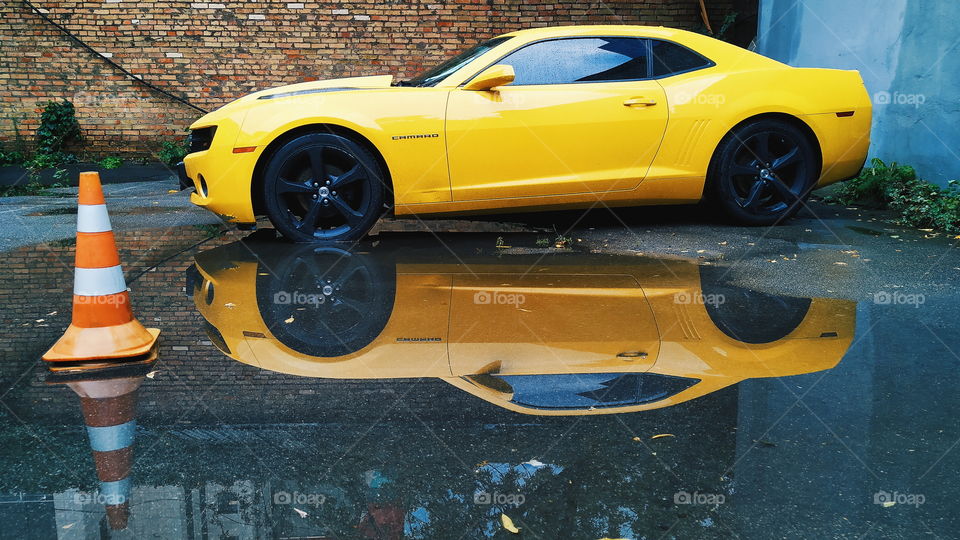 reflection of a yellow chevrolet car in a rain puddle