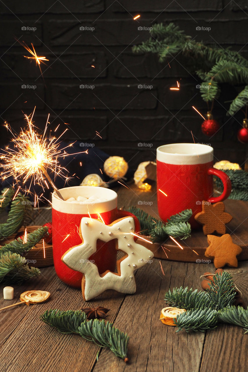 two cups of coffee and marshmallows, a burning Sparkler, gingerbread and fir branches.