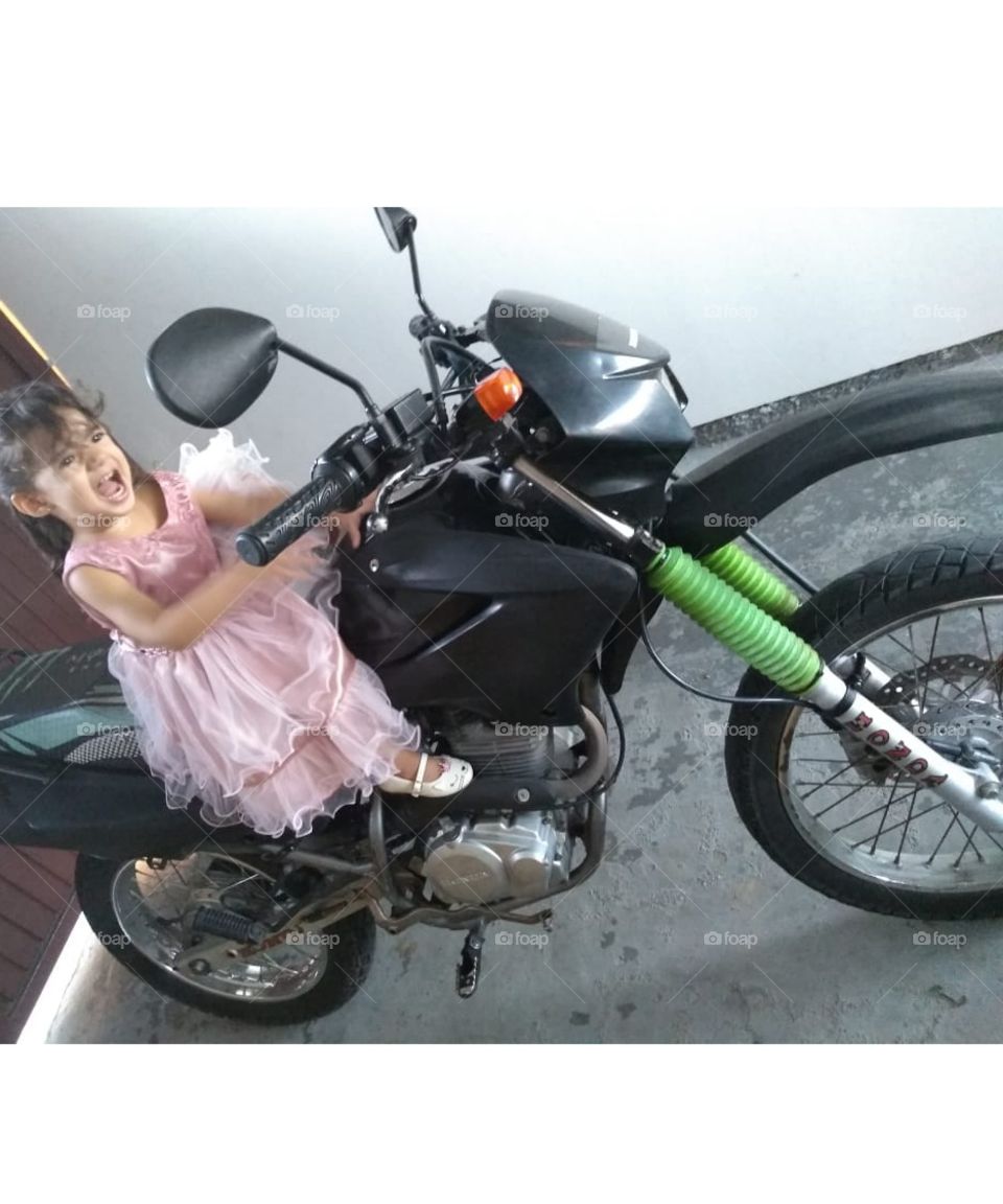 Menina de 2 anos está em cima de uma moto.