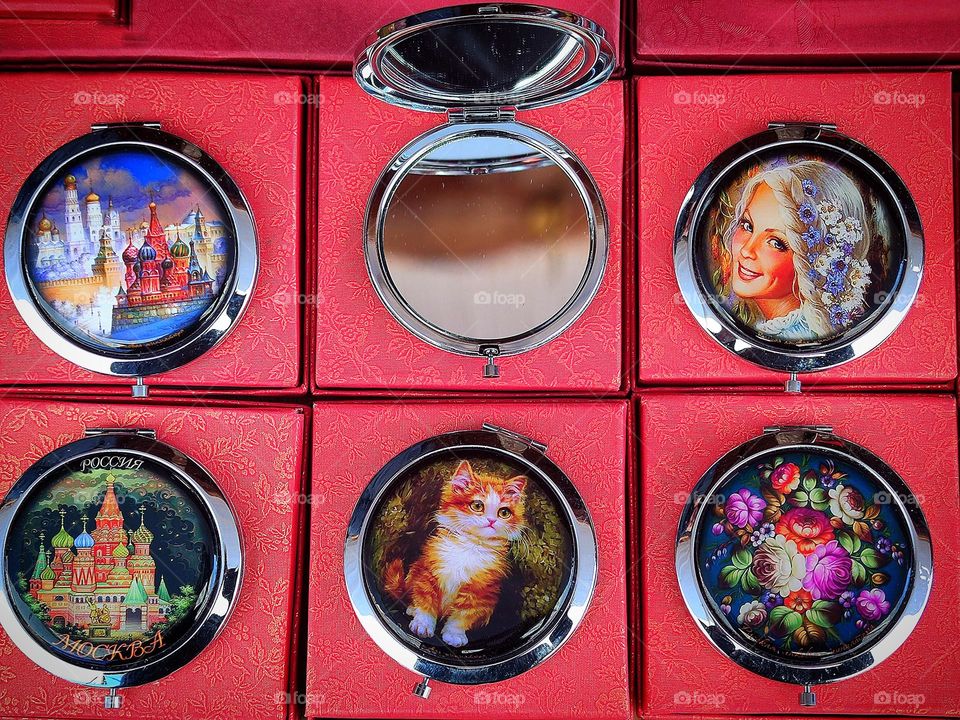 Circles. There are six round mirrors on the red boxes. One mirror is open. On the surface of five mirrors are various images of hand-made technique with enamel