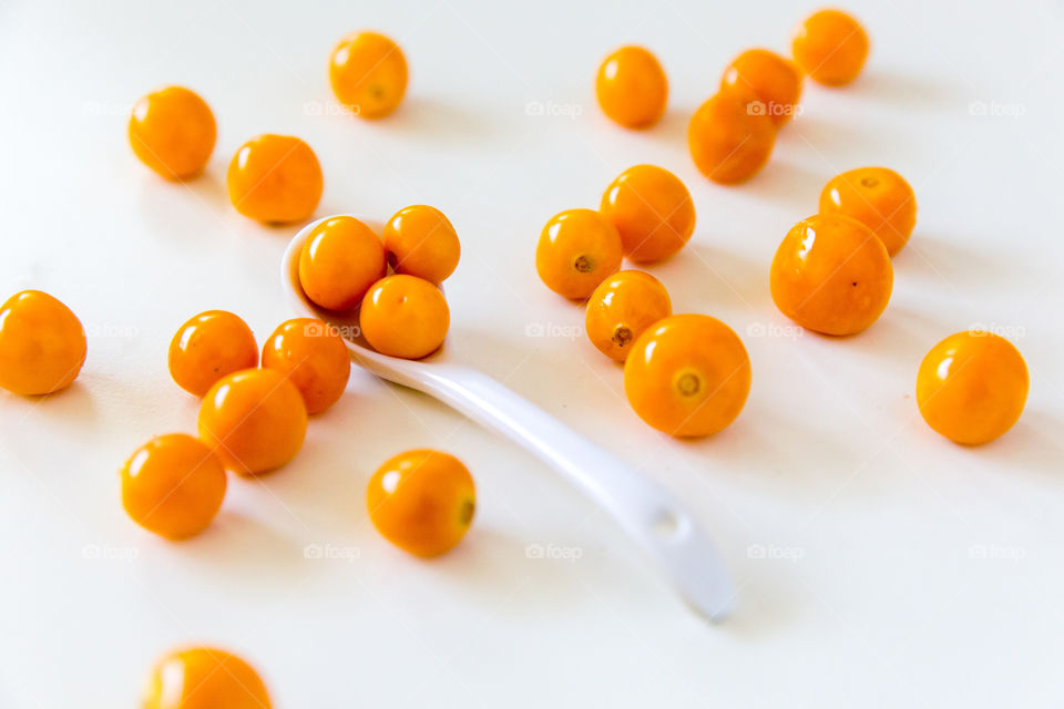 Fresh gooseberries on a white background with a single white spoon
 Fresh summer yellow fruit.