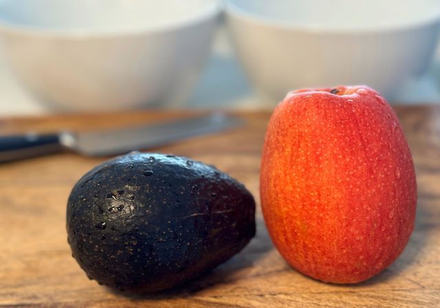 An avocado and an apple on a cutting board