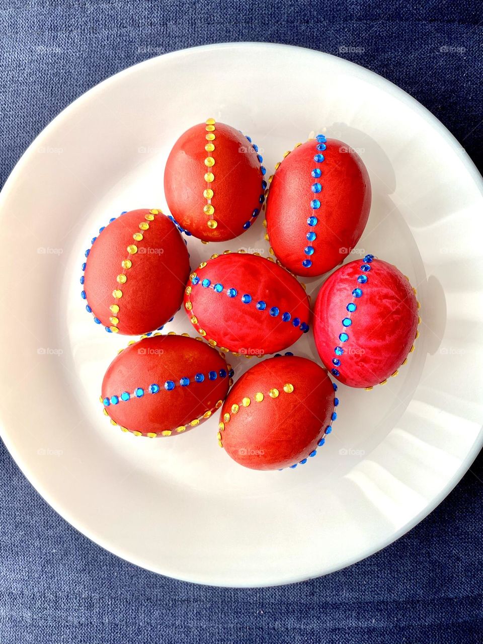 Easter red colored eggs decorated with yellow and blue rhinestones on white plate