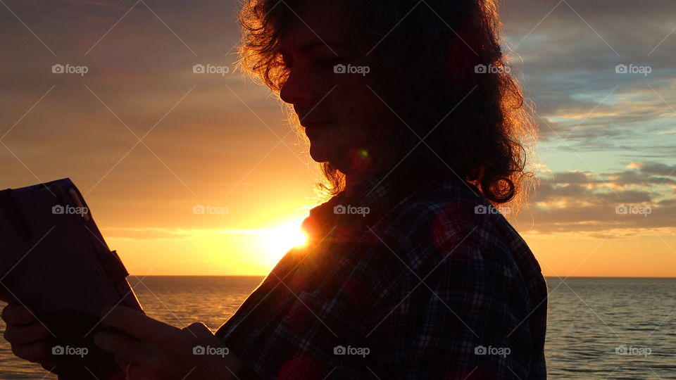 Woman silhouette profile against sunset at beach orange yellow one side turquoise gray other side