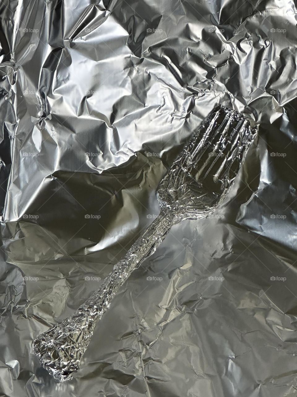 Silver plated salad fork wrapped in aluminum foil on crinkled foil background 