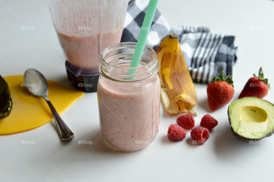 Fresh fruit smoothie in a glass with banana peel, avocado, strawberries, and raspberries