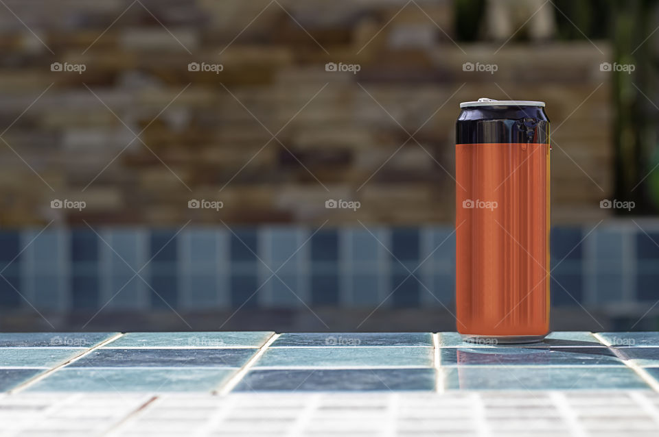 Canned drink red and  black on the tiled floor beside the pool.